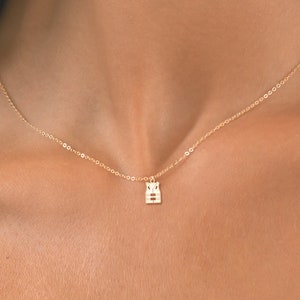 May include: A gold chain necklace with a small, geometric pendant. The pendant is a simple design with a square shape and a few lines.