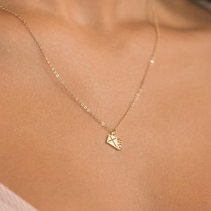 May include: A gold chain necklace with a small diamond-shaped pendant. The pendant has a delicate design of a letter inside.