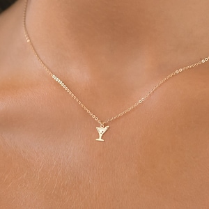 Puede incluir: Un collar de cadena dorada con un pequeño y delicado colgante de copa de martini.