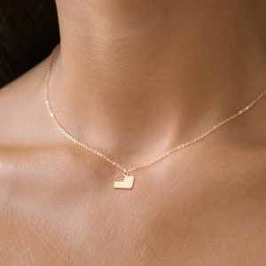 Puede incluir: Un collar de cadena de oro con un pequeño colgante cuadrado con un diseño de bandera estadounidense.