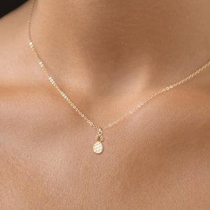 May include: A delicate gold chain necklace with a small, textured pineapple pendant.