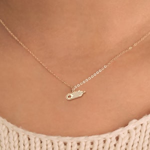 May include: A gold chain necklace with a small, delicate pendant shaped like a hand with outstretched fingers.