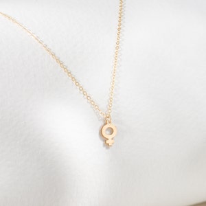 May include: A gold chain necklace with a small, delicate pendant in the shape of the female symbol.