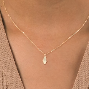Könnte beinhalten: Eine goldene Kettenkette mit einem kleinen Hamsa-Hand-Anhänger. Der Anhänger ist mit kleinen Diamanten verziert.