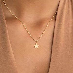 May include: A gold chain necklace with a small gold star pendant. The star has the word "SHERIFF" engraved on it.