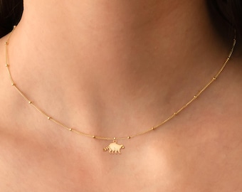 Könnte beinhalten: Eine goldene Kettenkette mit einem kleinen, zarten Anhänger in Form eines Faultiers. Die Kette wird von einem Model getragen.