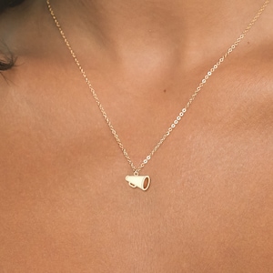 May include: A gold chain necklace with a small gold megaphone pendant.