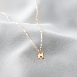 May include: A gold chain necklace with a wolf pendant. The necklace is on a white fabric background.