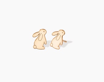 May include: A pair of gold-toned bunny rabbit stud earrings. The earrings are made of metal and have a simple, minimalist design.