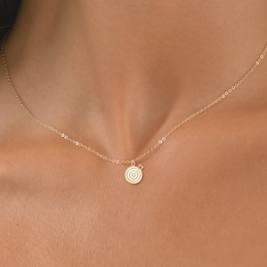 May include: A gold chain necklace with a small, circular pendant featuring a concentric circle design.