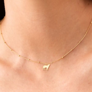 May include: A gold necklace with a small wolf pendant. The necklace is made of a delicate chain with small beads.