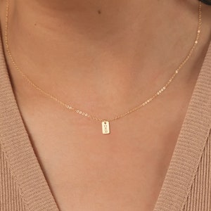 May include: A gold chain necklace with a small rectangular pendant that says "DKR" on it.