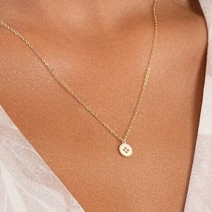 Op de afbeelding: Een delicate gouden ketting met een klein, rond hangertje in de vorm van een knoop.