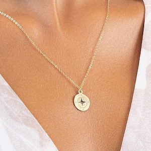 Puede incluir: Un collar de oro con un colgante de brújula. La brújula tiene una estrella negra en el centro.