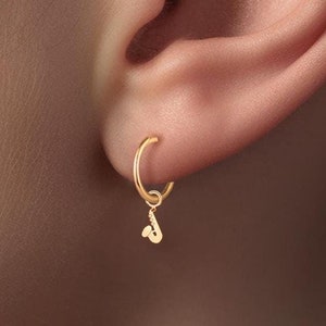 Pode incluir: Brincos de argola de ouro com um pequeno charme de saxofone pendurado em cada argola.
