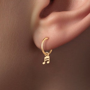 May include: Gold hoop earrings with a small music note charm hanging from the hoop.