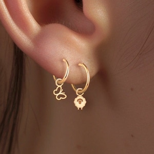 May include: Two gold hoop earrings with charms. The charm on the left is a butterfly and the charm on the right is a sheep.