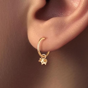 May include: Gold hoop earrings with a small cow charm hanging from the bottom.