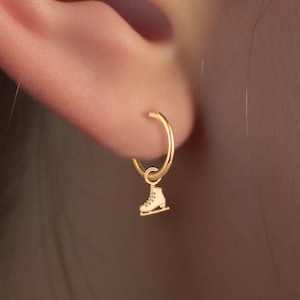 以下が含まれることがあります： 金色のフープピアスに、小さな金色のスケート靴のチャームがぶら下がっています。