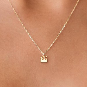 May include: A gold chain necklace with a small gold clapperboard pendant.