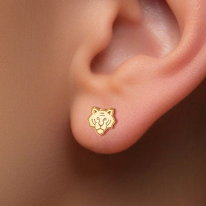 May include: Gold tiger head stud earrings. The earrings are small and delicate, and they feature a detailed tiger head design.