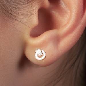 May include: A close-up of a person's ear with a small silver earring featuring a knot design.