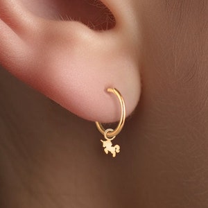 May include: Gold hoop earrings with a small unicorn charm hanging from the bottom.