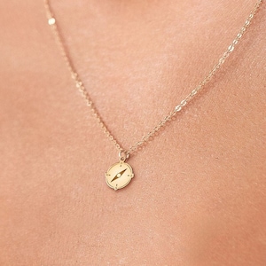 May include: A gold chain necklace with a small gold pendant featuring a compass design.