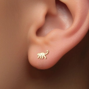 Può includere: Orecchini a lobo in oro a forma di scimmia. Gli orecchini sono piccoli e delicati, e la scimmia è rivolta a destra.
