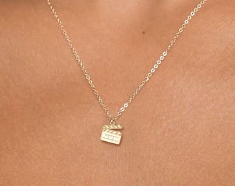 May include: A delicate gold-colored necklace featuring a small, textured pendant. The pendant is square-shaped and hangs from a fine chain. The necklace is worn around the neck, creating a simple and elegant look. The jewelry is likely made of gold.