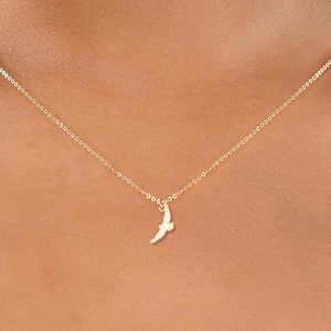 Op de afbeelding: Een delicate goudkleurige ketting met een kleine hanger in de vorm van een vogel in vlucht. De hanger hangt aan een fijne ketting, wat een minimalistische en elegante uitstraling creëert. De ketting wordt getoond tegen een neutrale achtergrond.