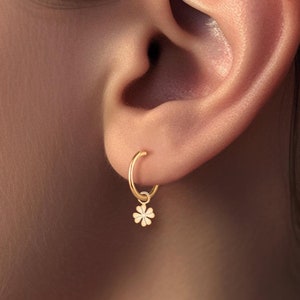 May include: Gold hoop earrings with a small four-leaf clover charm dangling from the bottom.