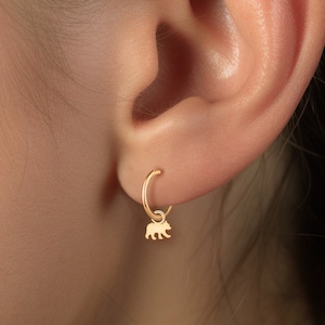May include: Gold hoop earrings with a small bear charm hanging from the bottom.