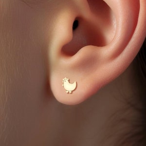 May include: A pair of gold earrings, one shaped like a small chicken and the other a small heart.