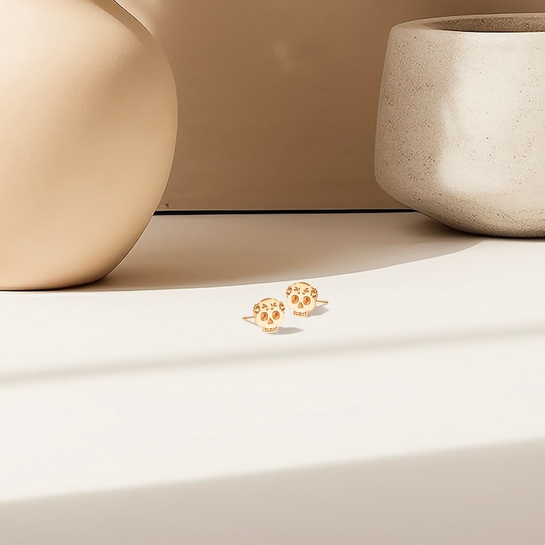 May include: A pair of gold-toned skull stud earrings. The skulls have a detailed design with small holes throughout.