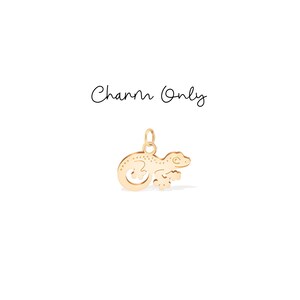 Pode incluir: Um berloque dourado em forma de lagarto. O berloque tem uma argola na parte superior para prender a um colar ou pulseira. O texto "Charm Only" está escrito acima do berloque em itálico.