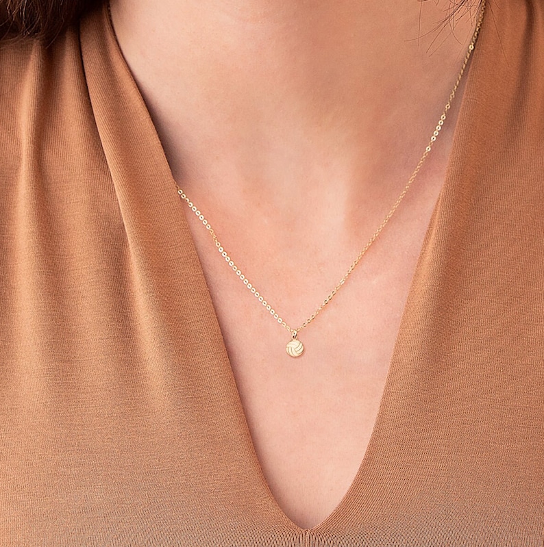 Pu&ograve; includere: Una collana con catena dorata con un piccolo ciondolo rotondo con un design a pallavolo.