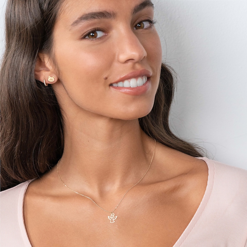 May include: A gold necklace with a delicate angel pendant. The necklace is worn by a person with long brown hair.