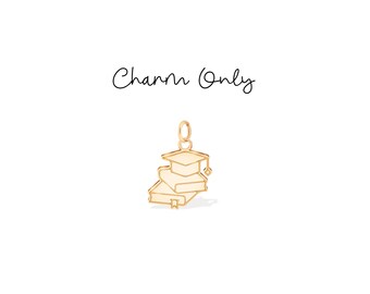 Könnte beinhalten: Ein goldfarbener Anhänger mit einer Abschlusskappe auf einem Stapel Bücher. Der Anhänger hängt an einer kleinen Schlaufe. Die Worte "Charm Only" sind in Schreibschrift über dem Anhänger geschrieben.