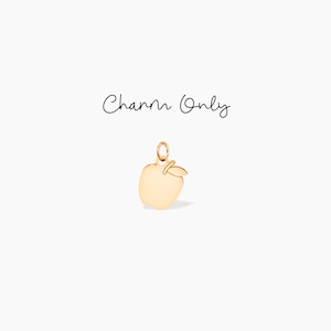 Puede incluir: Un charm de manzana de color dorado con un pequeño detalle de hoja. El charm está suspendido de un pequeño lazo. Las palabras "Charm Only" están escritas en cursiva encima del charm.