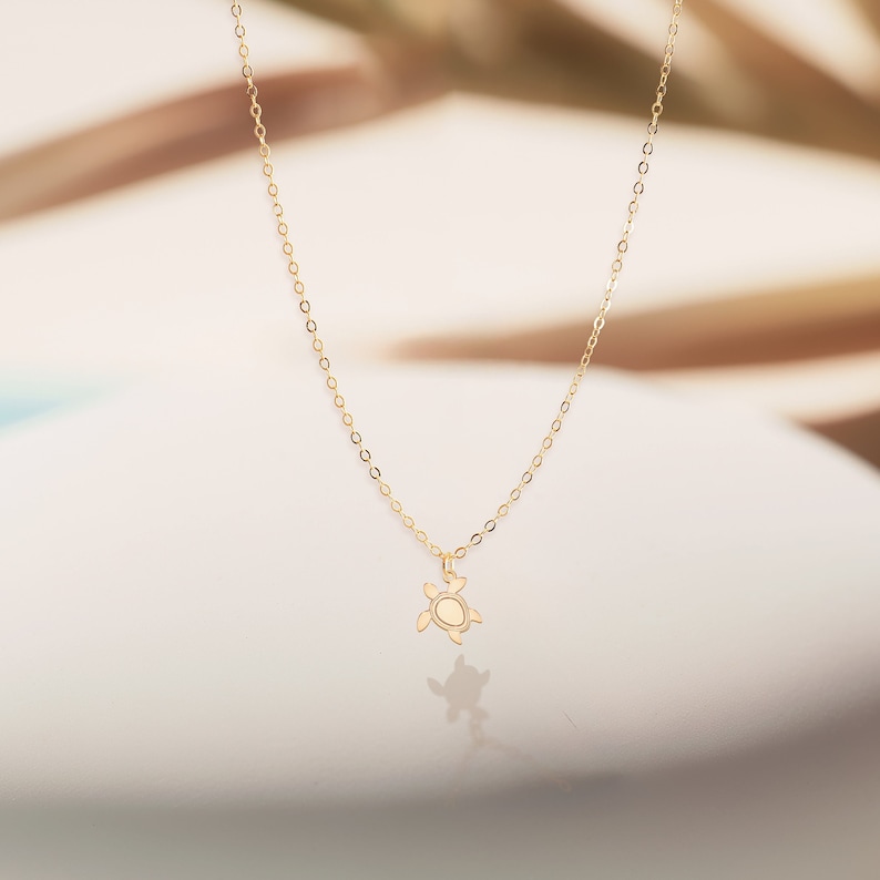 May include: A gold chain necklace with a small turtle pendant. The necklace is on a white background.