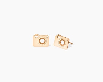 Op de afbeelding: Een paar gouden oorbelletjes in de vorm van een camera. De oorbelletjes zijn klein en delicaat, en ze zouden een geweldig cadeau zijn voor een fotograaf of iedereen die van fotograferen houdt.