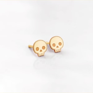 Puede incluir: Un par de pendientes de bot&oacute;n de calavera de color dorado. Las calaveras son peque&ntilde;as y tienen un dise&ntilde;o sencillo.