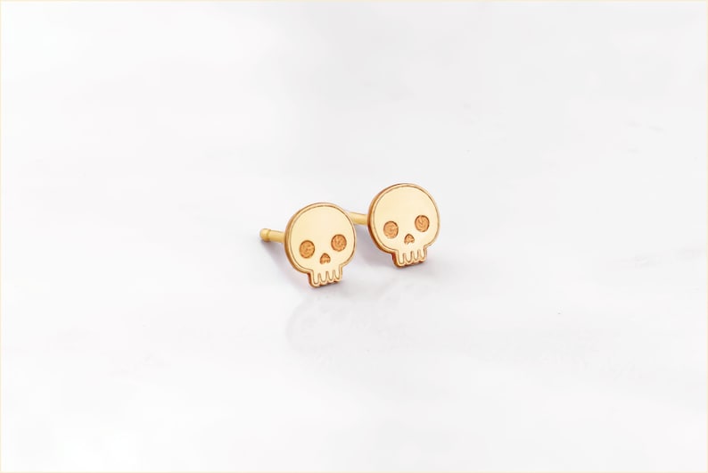 Puede incluir: Un par de pendientes de bot&oacute;n de calavera de color dorado. Las calaveras son peque&ntilde;as y tienen un dise&ntilde;o sencillo.