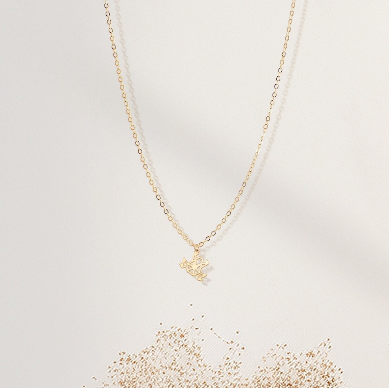 May include: A delicate gold chain necklace with a geometric pendant. The pendant is a stylized design of a bird in flight.