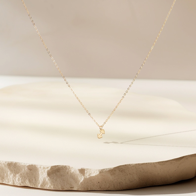 May include: A gold chain necklace with a small gold dumbbell pendant.