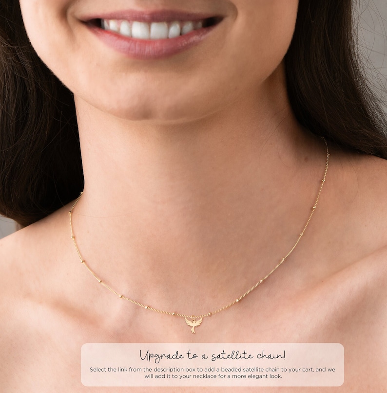 May include: A gold necklace with a small bird pendant. The necklace is on a model's neck. The text "Upgrade to a satellite chain! Select the link from the description box to add a beaded satellite chain to your cart, and we will add it to your necklace for a more elegant look." is below the image.