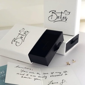 May include: Two white gift boxes with black lids and the word "Brites" printed on them. The boxes are open and a handwritten note is visible in the background. The note says "Sunshine, You are the love of my life and I am truly blessed to have you. Love S."