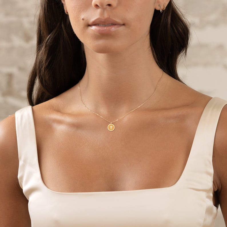This delicate gold charm pendant necklace features a minimalist circular design with a unique symbol, perfect for everyday wear or special occasions. Ideal for those who appreciate subtle elegance.