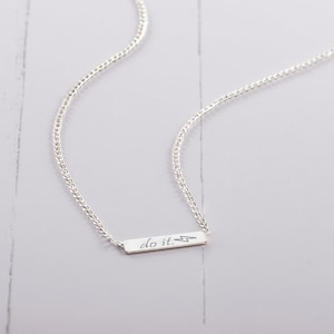 May include: A silver chain necklace with a small silver bar pendant that says "do it." with a lightning bolt symbol.
